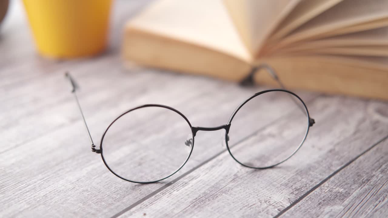 Libro abierto, gafas y taza de café sobre una mesa de madera