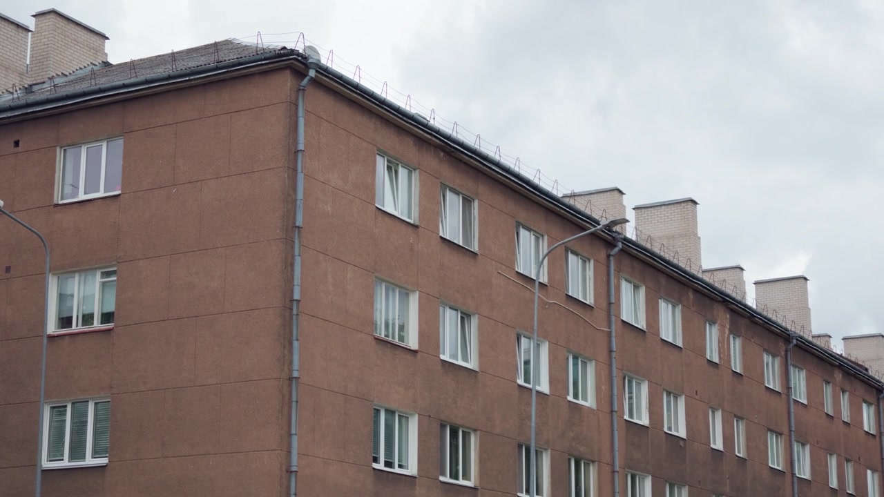 Utvendig bilde fra lav vinkel av en brun fasade på en boligblokk i flere etasjer bygget under sovjettiden i Daugavpils by under overskyet himmel, Latvia