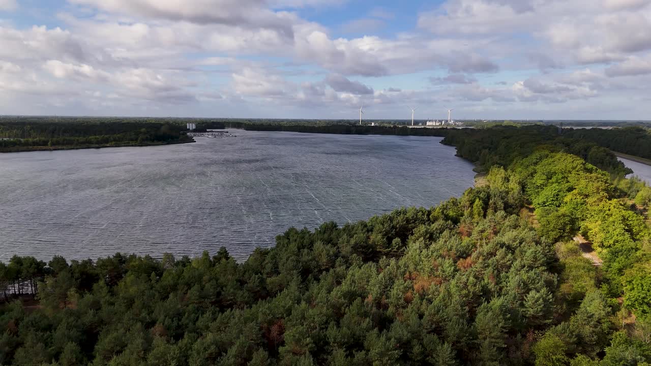 Vista aerea panoramica di un lago circondato da una foresta con turbine eoliche sullo sfondo