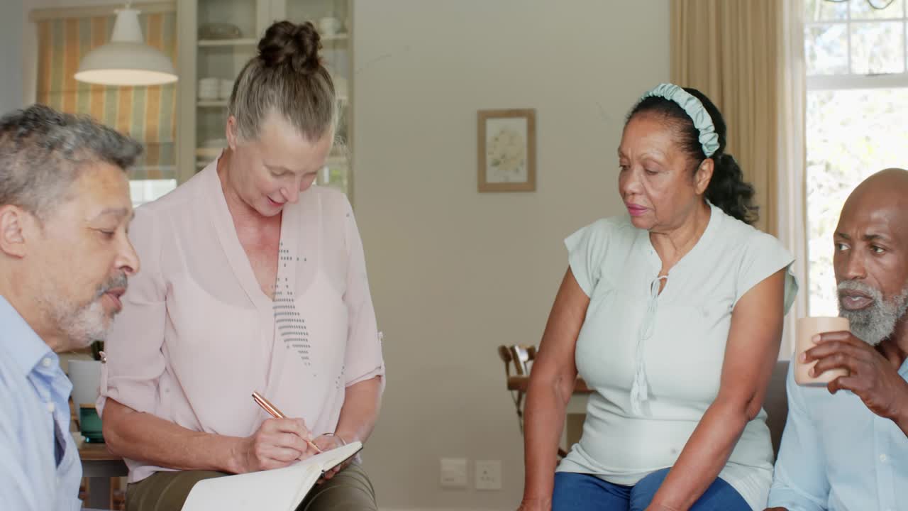 Woman in light pink leaning forward and reaching, guiding health talk while writing notes, pointing