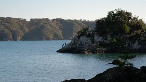 people fishing on small island with massive ship passing behind