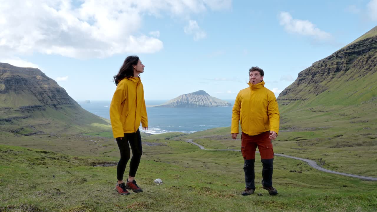 A couple in yellow jackets running through a lush valley in Faroe Islands joyfully