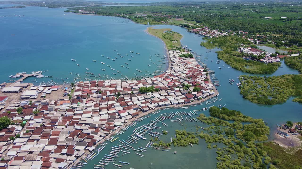 imágenes de drones de 4k de un activo puerto pesquero tradicional en lombok, con barcos en constante movimiento, numerosas embarcaciones atracadas, un denso pueblo y los bosques de manglares circundantes que mejoran la escena
