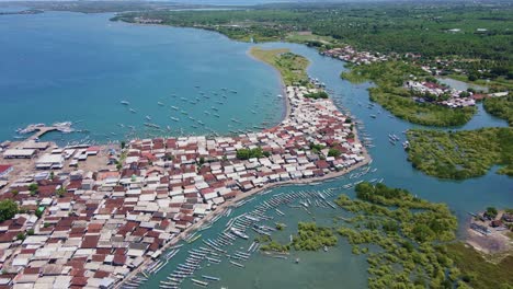 4k drone footage of a busy traditional fishing port in lombok, with boats constantly moving, numerous vessels docked, a dense village, and surrounding mangrove forests enhancing the scene