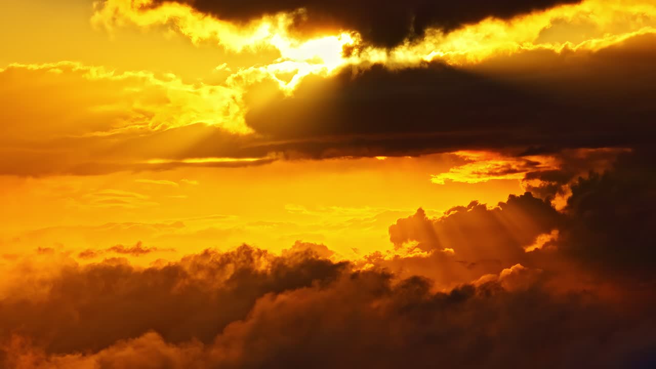 Goldene Sonnenstrahlen brechen durch schwere Wolken über einem leuchtenden Horizont und werfen dramatisches Licht über die obere Atmosphäre während eines ruhigen Sonnenuntergangs aus der Luft.