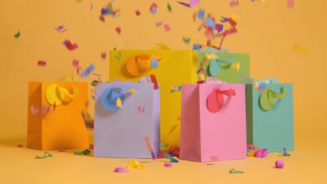 studio shot of colourful birthday party gift bags against yellow background with falling paper confetti