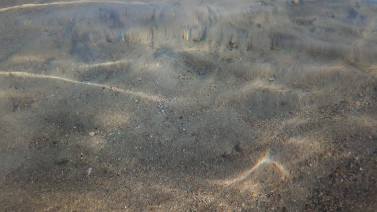 Calm underwater view showing sand ripples and light reflections beneath the sea surface