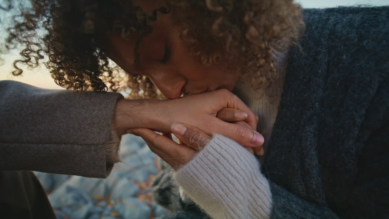 Enamoured brunette kissing man hands at romantic date on ocean coast closeup