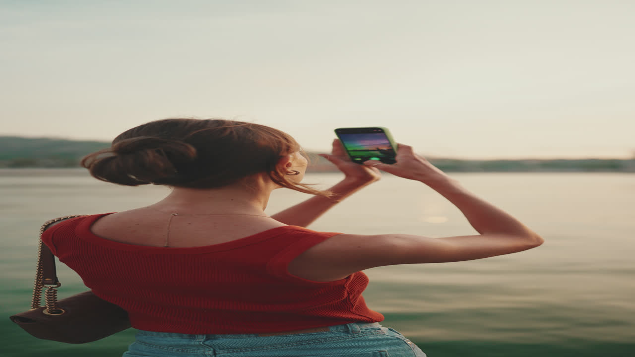 Woman taking picture with smartphone at sunset