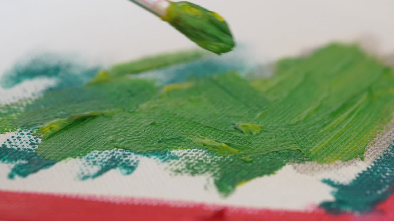 Close-up of a paintbrush applying green paint on canvas