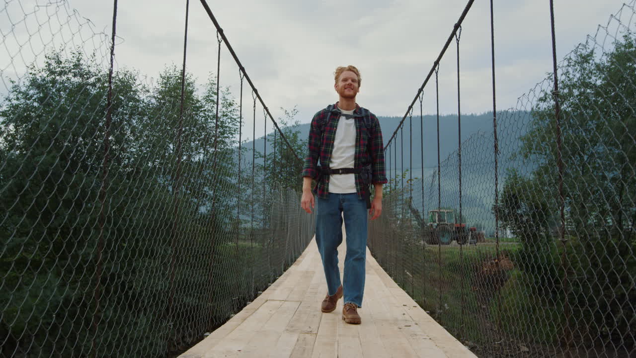 Uomo in viaggio cammina su un ponte tra le montagne di campagna. Ragazzo sorridente esplora la natura.