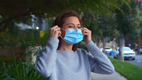 [camera used: canon c300] caucasian woman laughing and happy outdoors puts on a surgical face mask