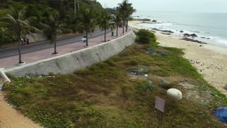 aerial view of surfer driving along the tropical asiatic scenic coastline carrying a surf board with modern scooter sealinks, vietnam