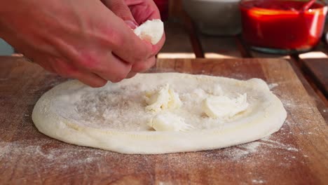 caucasian hands pulls apart mozzarella cheese and tops traditional italian pizza