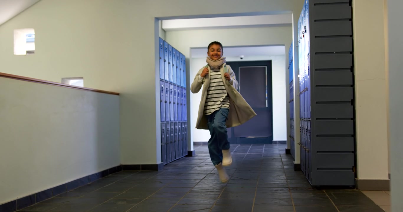 Teenager afrikansk-amerikansk pige træder ind i skolens gang fra døråbningen, skynder sig til time med rygsækken i et fast greb.