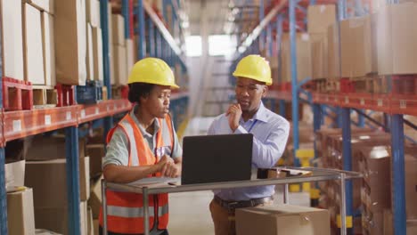 Trabajadores-Afroamericanos,-Hombres-Y-Mujeres,-Con-Casco-Y-Usando-Una-Computadora-Portátil-En-El-Almacén