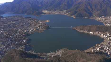 ciudad cerca de un lago rodeado de montañas en japón con un puente que cruza el área del agua durante el día