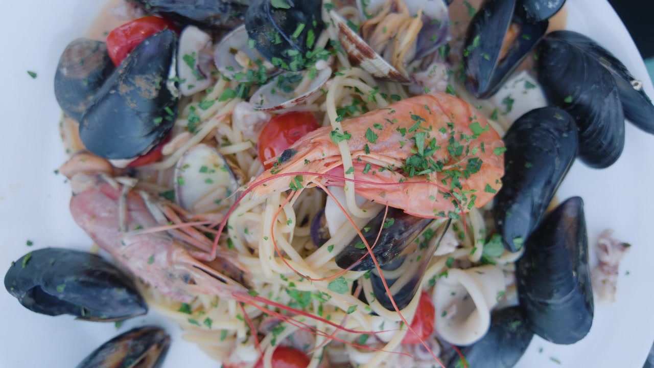 Primo piano di una pasta ai frutti di mare con cozze, vongole, gamberi e pomodorini su un piatto bianco