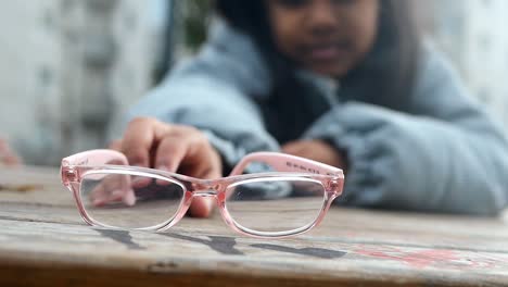 chica alcanzando gafas rosadas en una mesa de madera