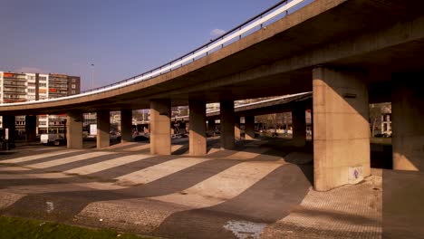 aerial sideways movement through large concrete overpass columns of highway intersection in urban surrounding