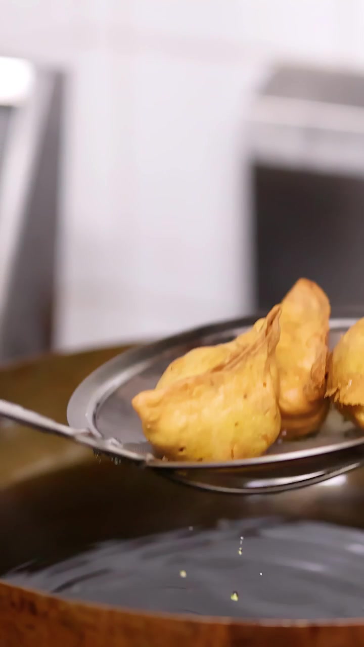Primo piano di samosa dorati sollevati dall'olio caldo con una schiumarola in una cucina di Bangkok.