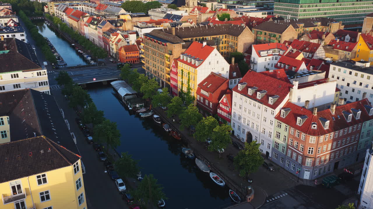 Copenhagen, Denmark - August 3, 2025: Aerial drone view of the Nyhavn Canal lined with colourful historic buildings, red rooftops, and moored boats