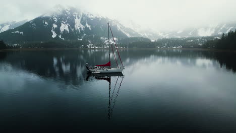 Aerial-view-circling-a-sailboat-in-tranquil-waters,-under-snowy-mountains-of-Alaska