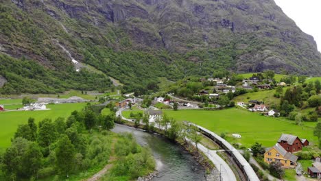 aerial: flåm train going through a valley among green meadows and by a river