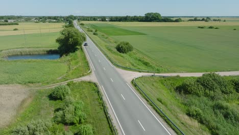 aerial establishing shot of a rural landscape, countryside road with trucks and cars moving, lush green agricultural crop fields, sunny summer day, wide drone shot