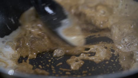 mixing dark massaman curry paste with fresh coconut milk in non stick pan - close up