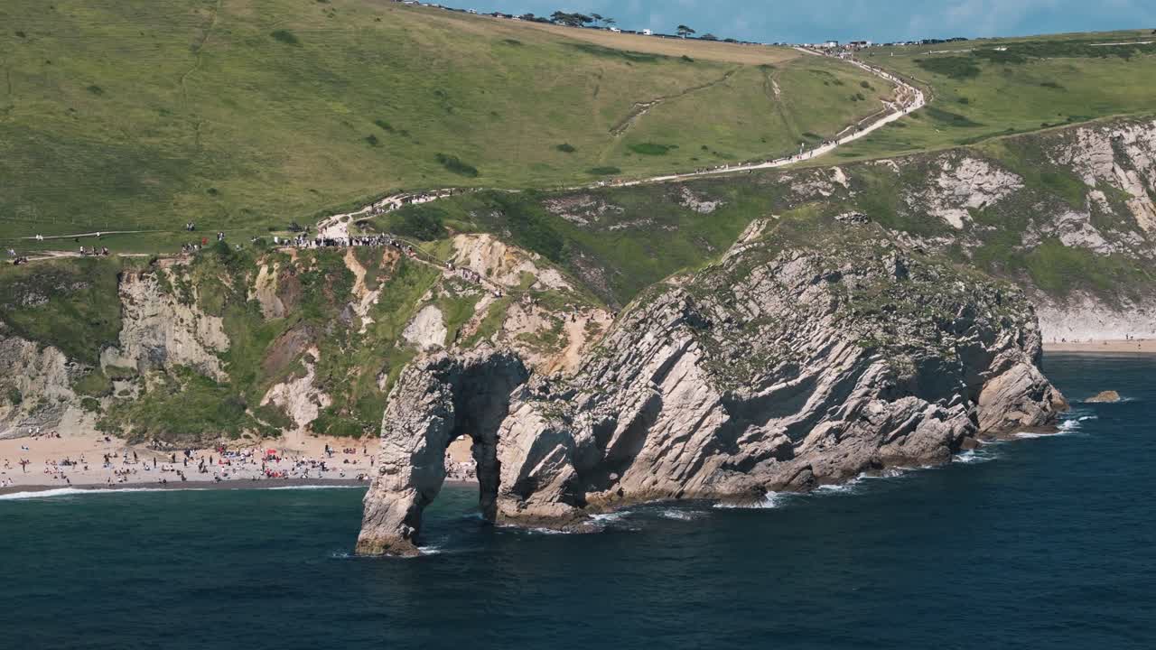 Low circle drone around Durdle Door showing rock formation, ocean, and beach curve