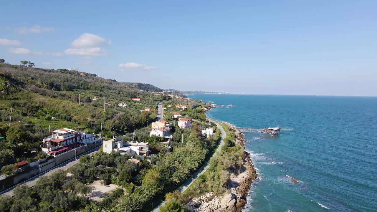 Yeşil yamaçlara yerleşmiş beyaz binaları, turkuaz Adriyatik Denizi, kayalık sahil şeridi ve uzaktaki ufuk manzarası ile Abruzzo sahil köyünün geniş açılı hava görünümü.