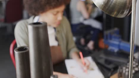 busy biracial female worker drawing design of jewellery in jewellery studio in slow motion