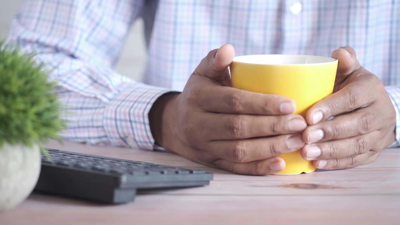 Person holder en gul kaffekop ved sit skrivebord