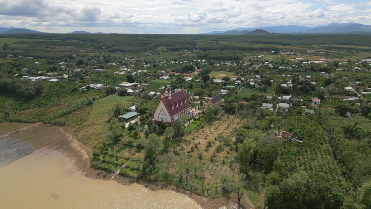 Rød katolsk kirke omgivet af landbrugsjord og afgrødemarker i Centralvietnam ved Dak Bla-floden. Drone cirkulerer 4K 30FPS.