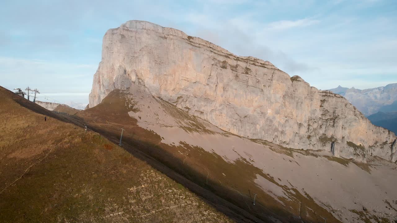 Aerial flyover alongside the cliffs of Tour d'A&iuml; and slopes of Leysin in Vaud, Switzerland with les Diablerets in view during a colorful autumn afternoon in the Swiss Alps