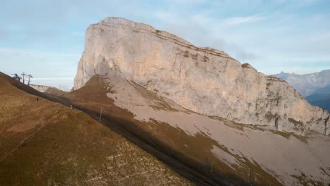 aerial flyover alongside the cliffs of tour d'aï and slopes of leysin in vaud, switzerland with les diablerets in view during a colorful autumn afternoon in the swiss alps