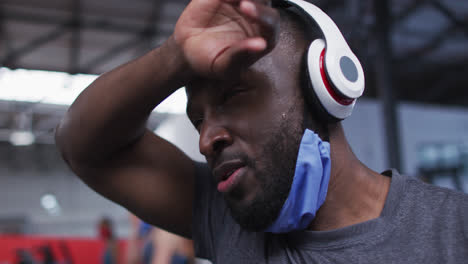 African-american-man-wearing-lowered-face-mask-exercising-at-gym