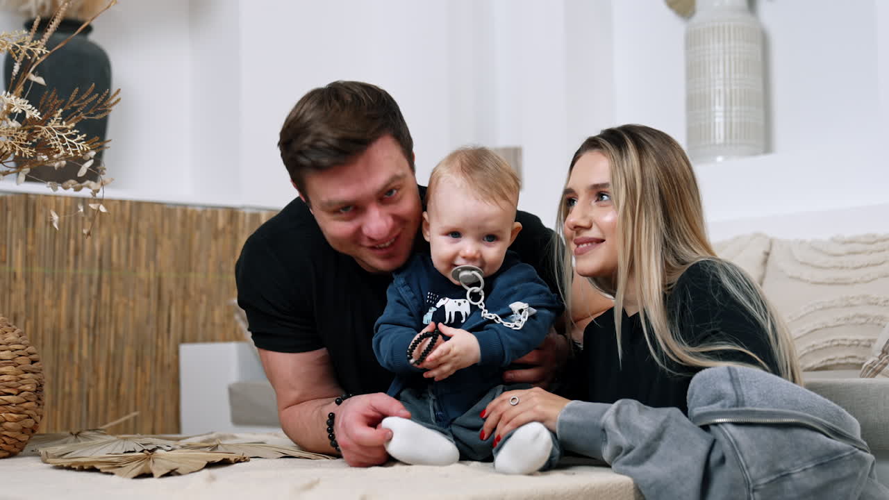 Beautiful Caucasian family of three at home. Loving parents kiss their son busy with bracelet.
