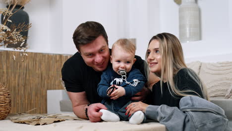 beautiful caucasian family of three at home. loving parents kiss their son busy with bracelet.