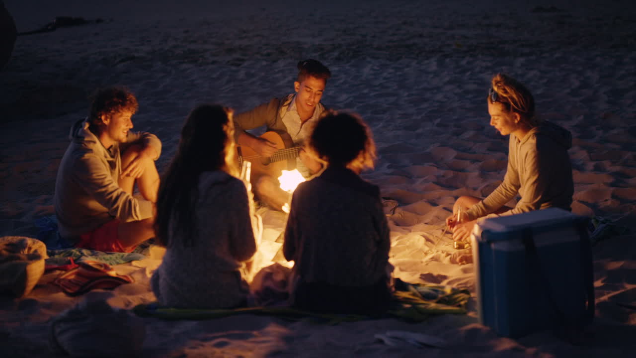 amigos cantando canciones alrededor de una fogata en la playa por la noche