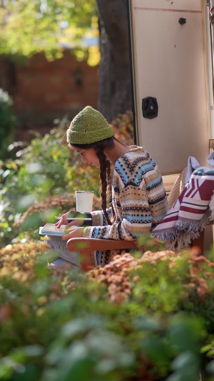 Donna che si rilassa in un camper, scrivendo su un quaderno, con paesaggio autunnale
