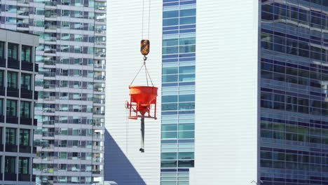 cubo naranja con hormigón colgado de una grúa frente a nuevos edificios con ventanas