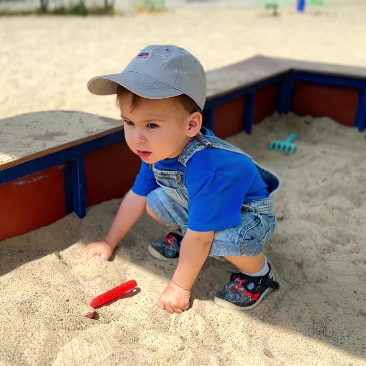 Tiny baby boy plays in a sandbox. Child holds his hands in the sand but looks around