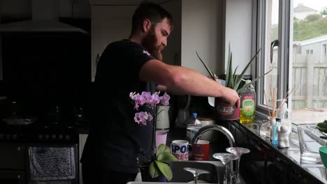 hombre barbudo riega las plantas de su casa