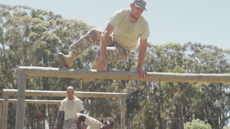 Diverse-group-of-male-soldiers-going-over-and-under-hurdles-on-army-obstacle-course-in-field