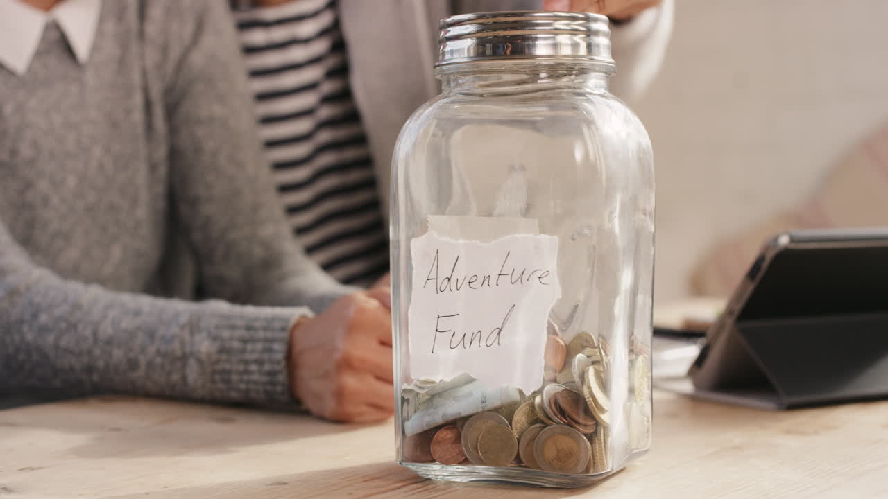 Happy mixed race couple saving money in adventure fund jar