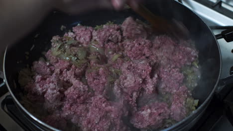 raw minced meat being stirred with wooden spoon in large frying pan