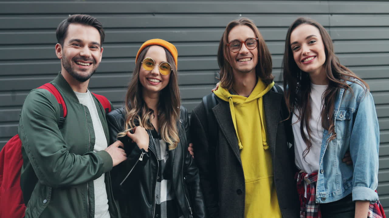 Portrait shot of caucasian young group of friends posing on a wall and smiling to the camera in the street
