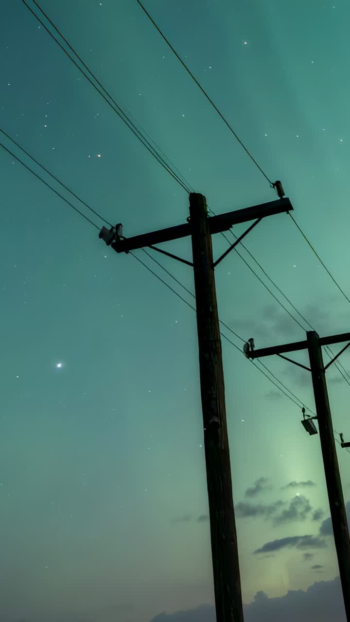 Vertical video: Panning camera starting revealing wooden pole at night, showing wires and stars